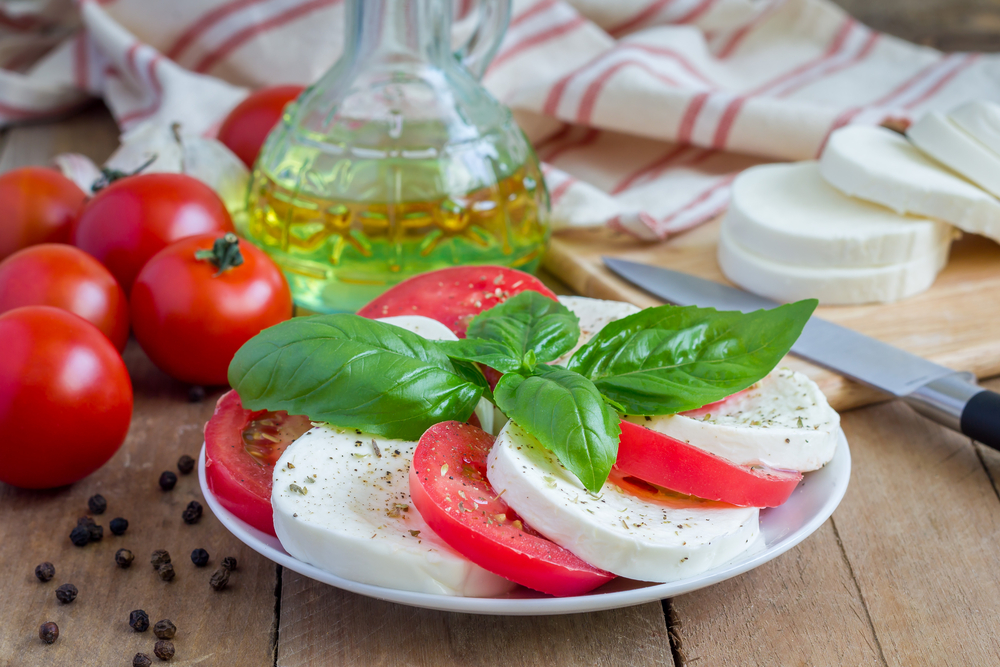 caprese salad with tomato, mozzarella and fresh basil leaves with bottle of olive oil to feature how herbs and olive oil enhance your dish